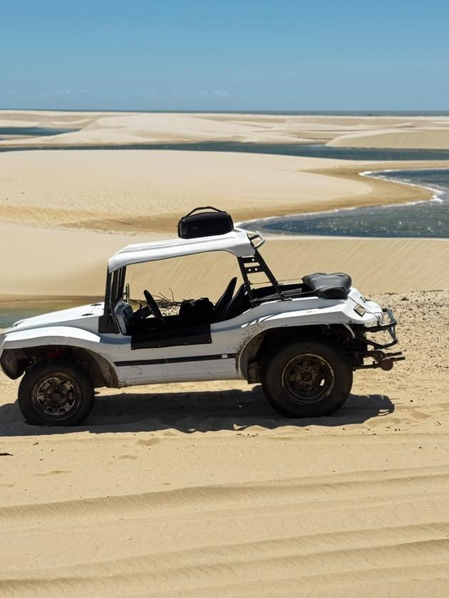 Buggy branco parado no alto das dunas dos Pequenos Lençóis, com lagoas e o mar ao fundo