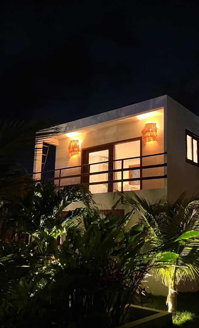 Fachada da Suíte Buriti à noite, iluminada, entre a vegetação