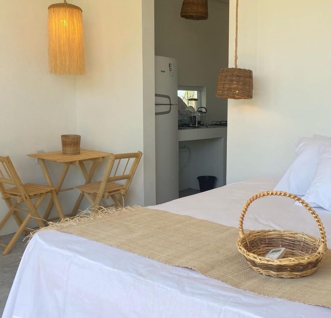Quarto com mesa de madeira, cadeiras e cama ao fundo