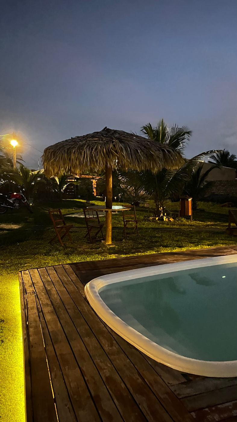 Piscina iluminada à noite, com quiosque de palha ao fundo