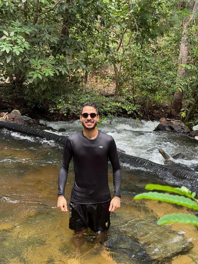 Visitante em pé nas águas rasas do rio, cercado pela mata
